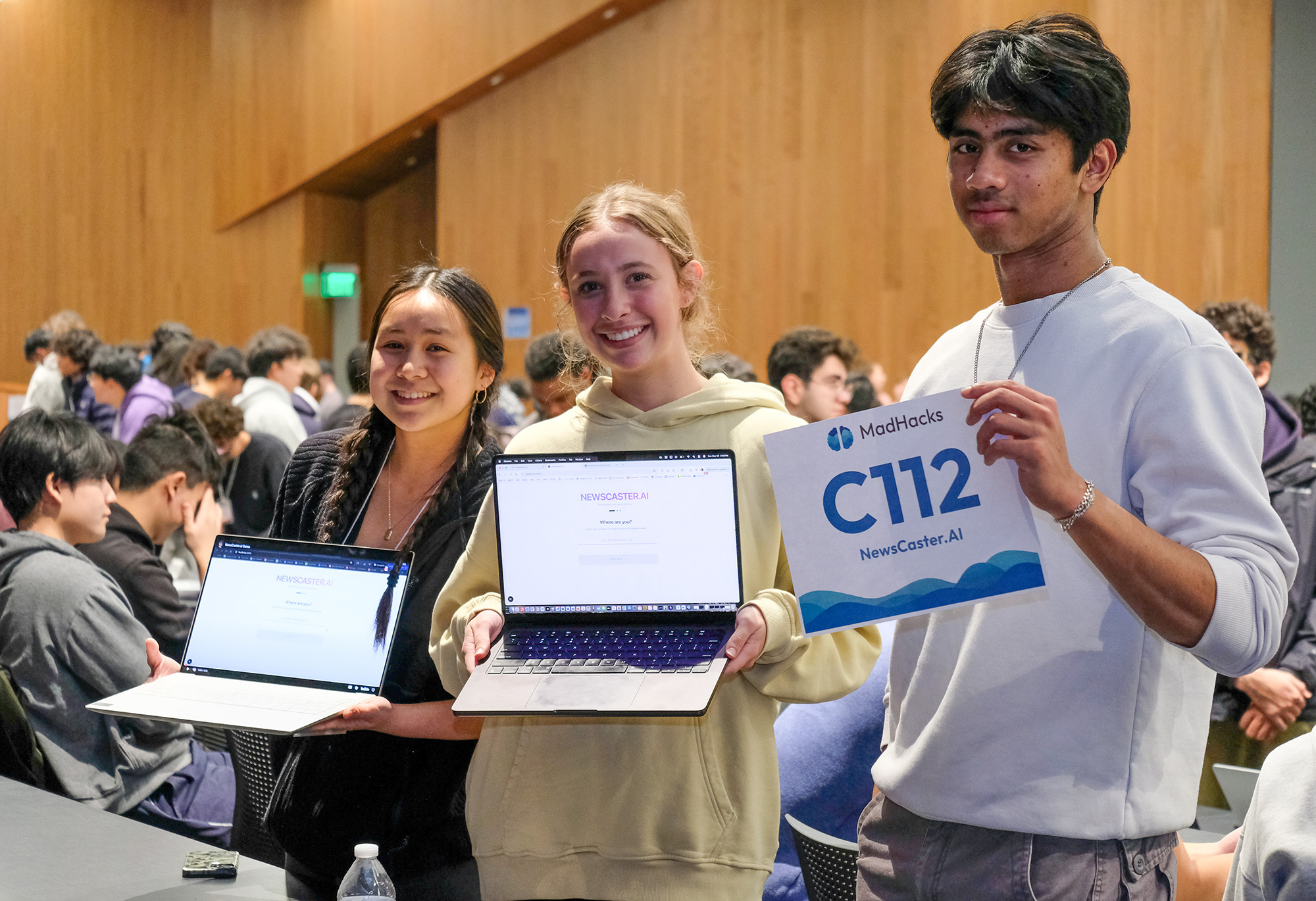 A MadHacks team poses with a sheet that says 'C112, NewsCaster dot AI'